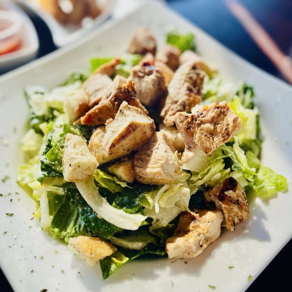 A close-up of a Caesar salad with grilled chicken and croutons on a white plate.