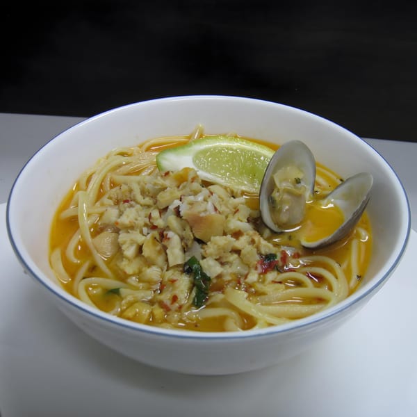Cajun seafood pasta with clams, crab meat, and a lime wedge in a white bowl.