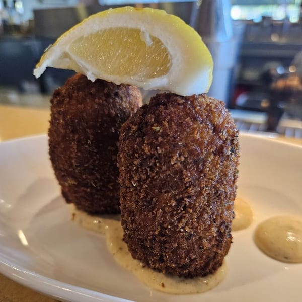 Two crispy, dark brown Cajun boudin balls with sauce and a lemon wedge on a white plate.