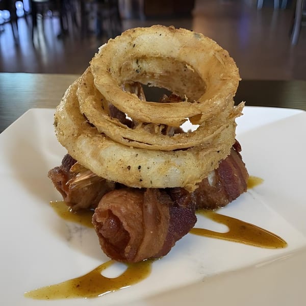 Cajun bacon-wrapped shrimp topped with crispy onion rings and a drizzle of sauce on a white plate.