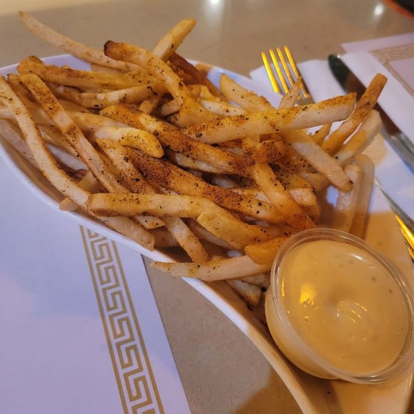 Cajun-seasoned french fries in a white bowl with a side of dipping sauce, fork, and knife.