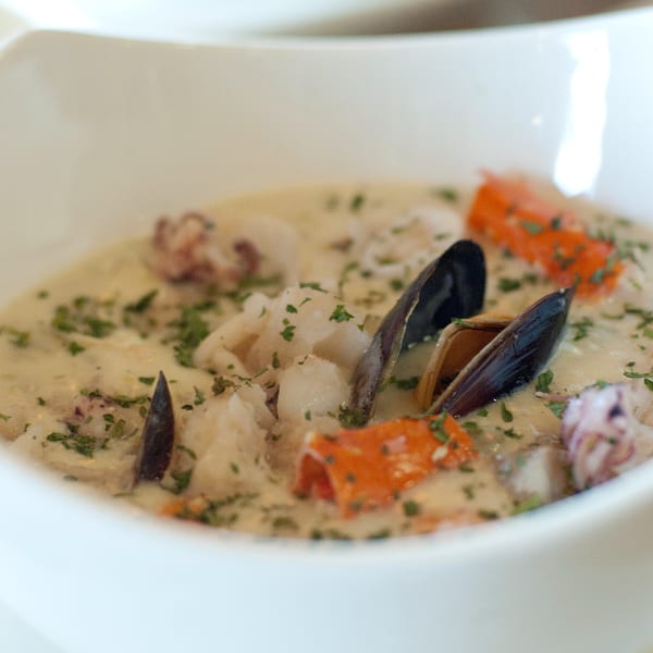 Close-up of a creamy Cajun seafood dish with mussels, shrimp, and red peppers in a white bowl.